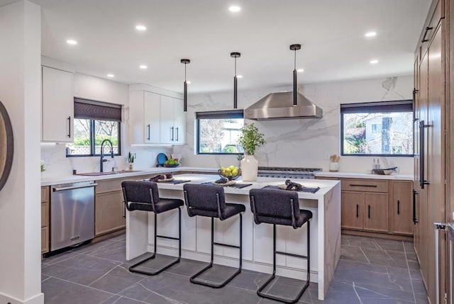 kitchen featuring a center island, sink, hanging light fixtures, stainless steel appliances, and wall chimney exhaust hood