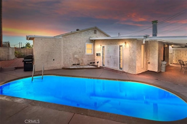 pool at dusk with a patio area and grilling area