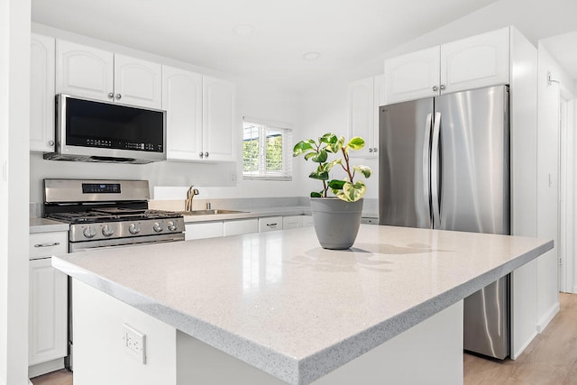 kitchen with sink, appliances with stainless steel finishes, white cabinetry, light stone countertops, and a kitchen island