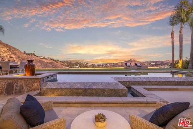 patio terrace at dusk with a mountain view and a pool with hot tub