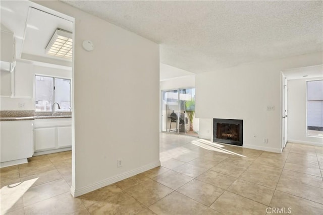 unfurnished living room with a textured ceiling, light tile patterned floors, and sink