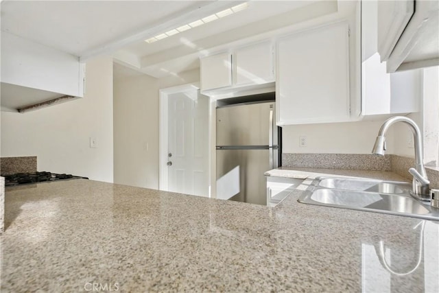 kitchen with white cabinetry, gas cooktop, stainless steel refrigerator, light stone counters, and sink