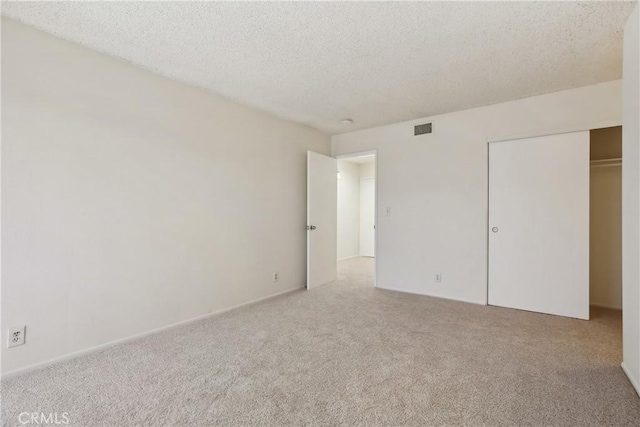 unfurnished bedroom featuring light colored carpet, a textured ceiling, and a closet