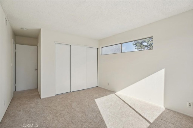 unfurnished bedroom with a textured ceiling, a closet, and light carpet