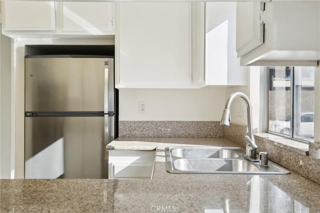 kitchen with light stone countertops, sink, white cabinetry, and stainless steel fridge