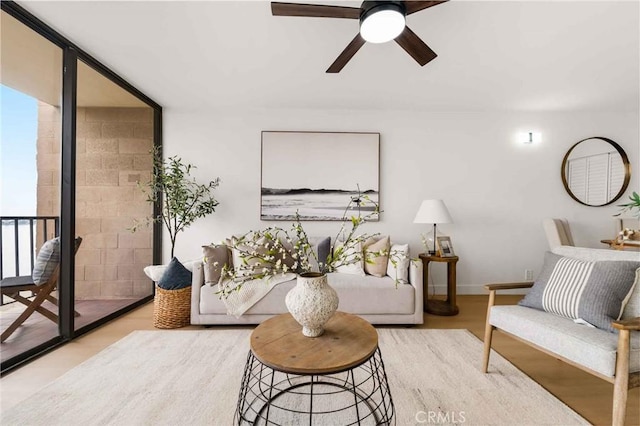 living room with ceiling fan, a wall of windows, and light wood-type flooring