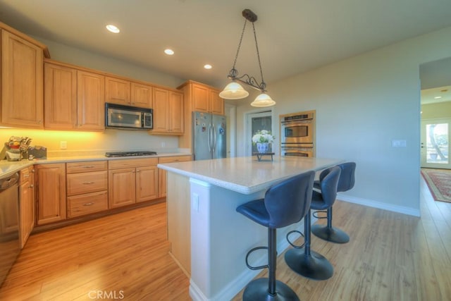 kitchen with decorative light fixtures, appliances with stainless steel finishes, light hardwood / wood-style flooring, and a kitchen island