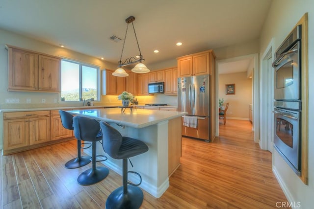 kitchen featuring a center island, decorative light fixtures, a kitchen bar, stainless steel appliances, and light wood-type flooring