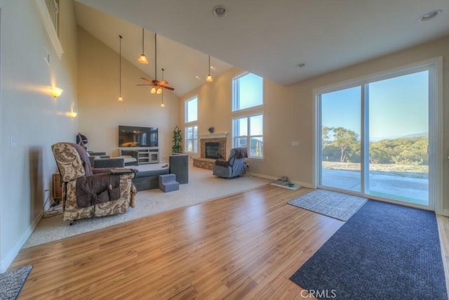 living room with ceiling fan, light wood-type flooring, a brick fireplace, and a high ceiling