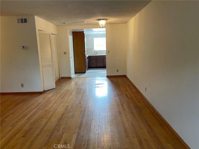 empty room featuring light wood-type flooring, a textured ceiling, and sink