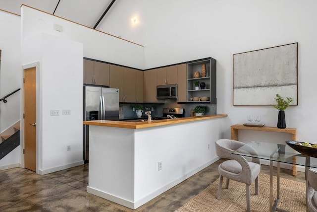 kitchen featuring kitchen peninsula, stainless steel appliances, a towering ceiling, and concrete flooring