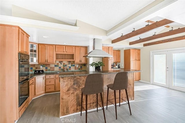 kitchen with island range hood, hardwood / wood-style floors, backsplash, lofted ceiling, and a kitchen island