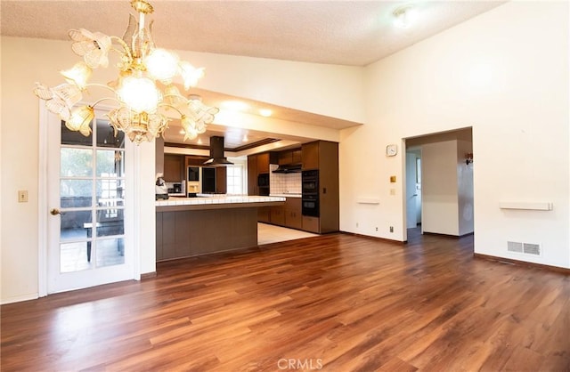 kitchen with dark brown cabinetry, dark wood-type flooring, island range hood, kitchen peninsula, and a notable chandelier