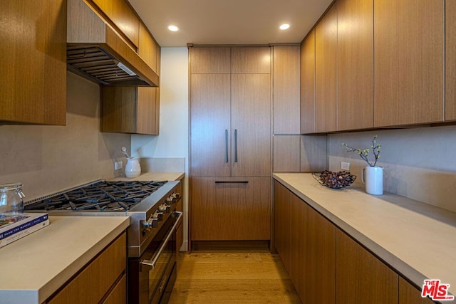 kitchen featuring high end stove, light wood-type flooring, and wall chimney exhaust hood