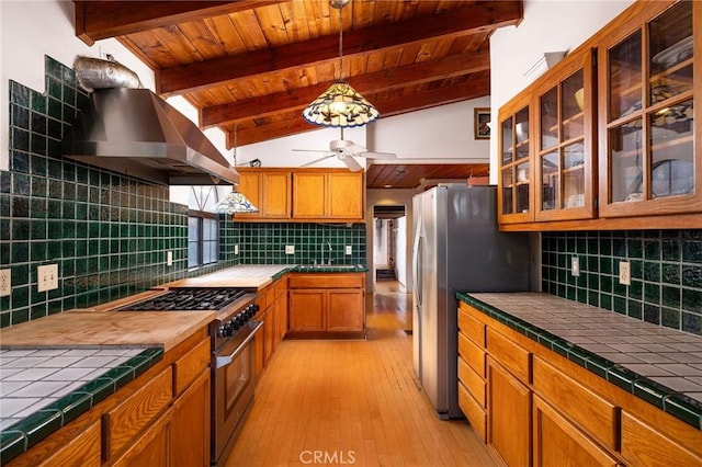 kitchen with extractor fan, tasteful backsplash, lofted ceiling with beams, tile counters, and stainless steel appliances