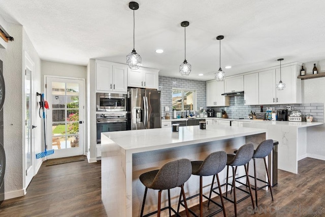 kitchen featuring decorative light fixtures, a kitchen breakfast bar, white cabinets, stainless steel appliances, and backsplash