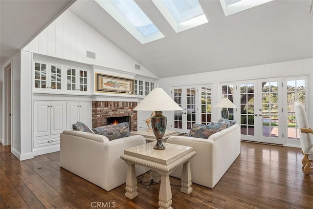 living room featuring dark hardwood / wood-style flooring, a skylight, french doors, high vaulted ceiling, and a brick fireplace