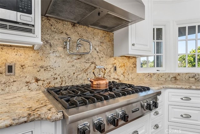 kitchen featuring light stone countertops, white cabinets, wall chimney range hood, backsplash, and stainless steel gas cooktop