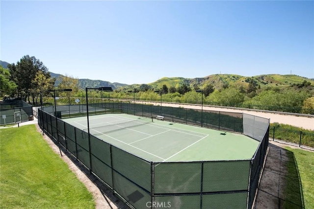 view of tennis court featuring a mountain view and a yard