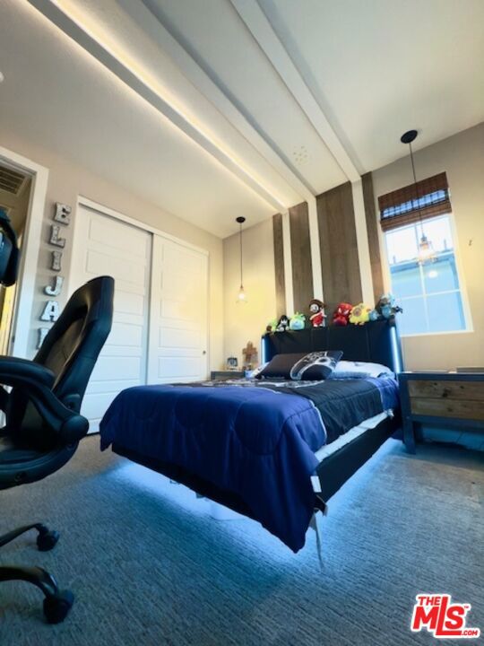 carpeted bedroom with a closet and beam ceiling