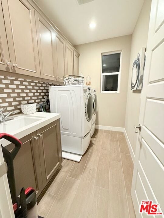 clothes washing area with sink, washer and dryer, light hardwood / wood-style floors, and cabinets