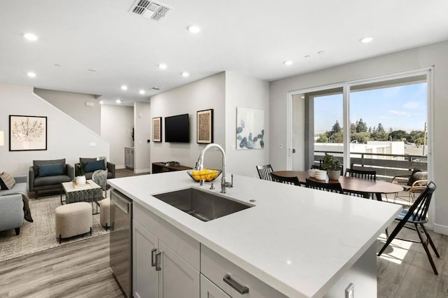 kitchen with a center island with sink, light wood-type flooring, dishwasher, white cabinets, and sink