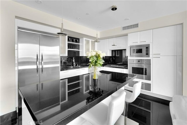 kitchen with built in appliances, dark countertops, visible vents, and a sink