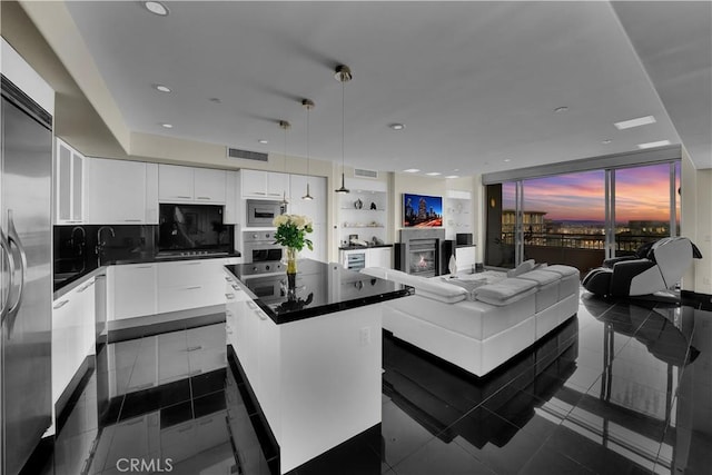 kitchen with built in appliances, dark countertops, a kitchen island, and visible vents