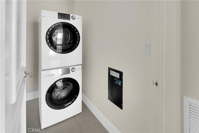 clothes washing area featuring baseboards, stacked washer / drying machine, tile patterned flooring, and laundry area