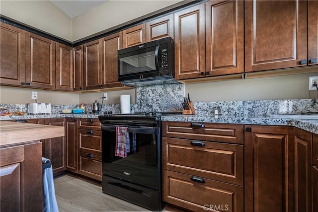 kitchen with light stone countertops, dark brown cabinetry, black appliances, and light wood-type flooring