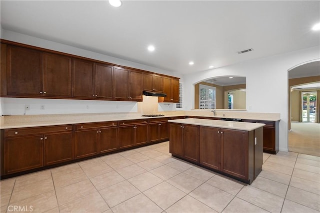 kitchen with dark brown cabinetry, stainless steel gas stovetop, light tile patterned flooring, and a center island