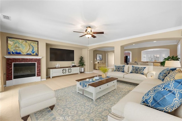 living room featuring ceiling fan, crown molding, and a fireplace