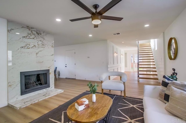 living room with ceiling fan, a large fireplace, and hardwood / wood-style floors