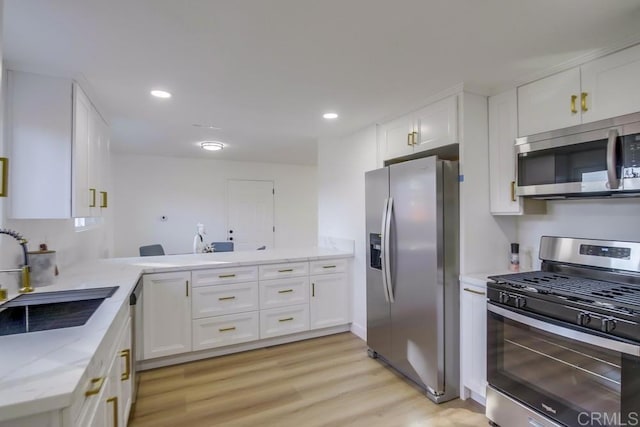 kitchen featuring kitchen peninsula, appliances with stainless steel finishes, light wood-type flooring, white cabinets, and sink