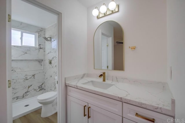 bathroom with toilet, vanity, wood-type flooring, and tiled shower