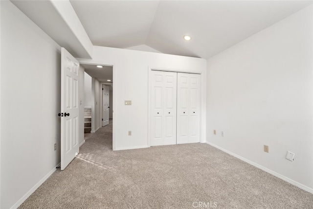 unfurnished bedroom featuring a closet, light colored carpet, and lofted ceiling