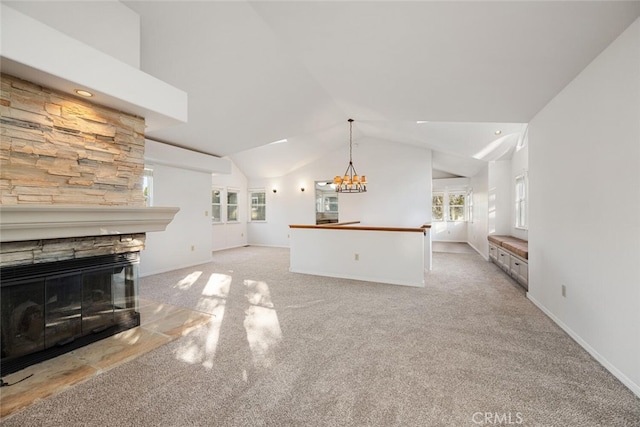 unfurnished living room with a notable chandelier, high vaulted ceiling, a stone fireplace, and light colored carpet