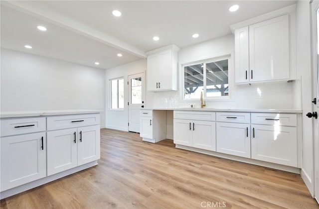 kitchen with light hardwood / wood-style floors, white cabinets, tasteful backsplash, and sink