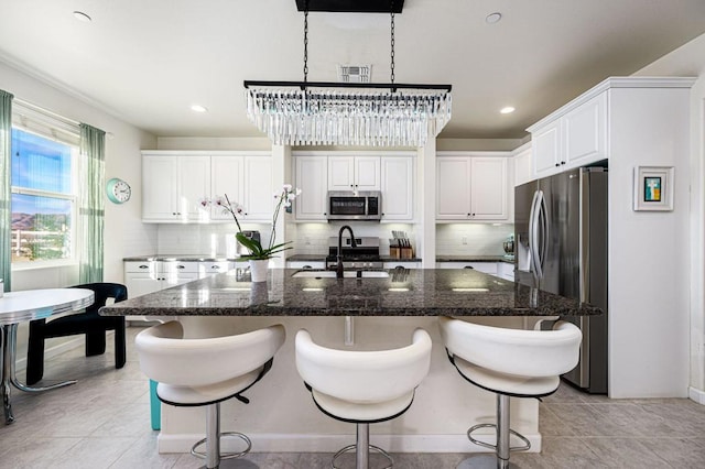 kitchen featuring decorative backsplash, sink, white cabinetry, a kitchen island with sink, and appliances with stainless steel finishes