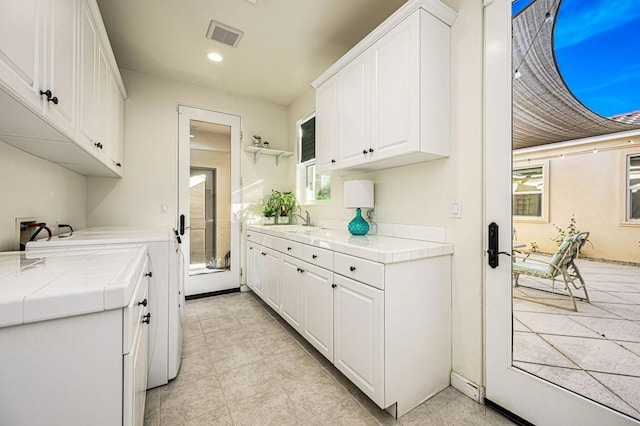 kitchen with tile countertops, white cabinetry, washer / clothes dryer, and sink