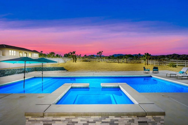 pool at dusk with an in ground hot tub and a patio