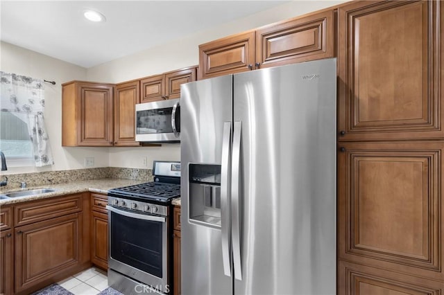 kitchen with light stone counters, sink, light tile patterned floors, and stainless steel appliances