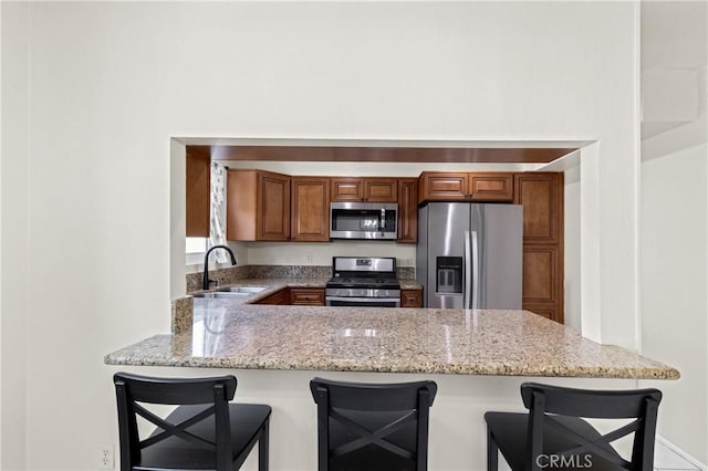 kitchen with a kitchen bar, stainless steel appliances, sink, kitchen peninsula, and light stone counters