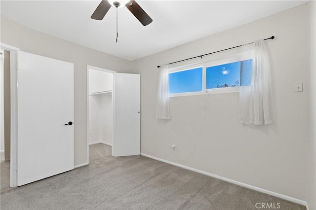 unfurnished bedroom with ceiling fan, a walk in closet, a closet, and light carpet