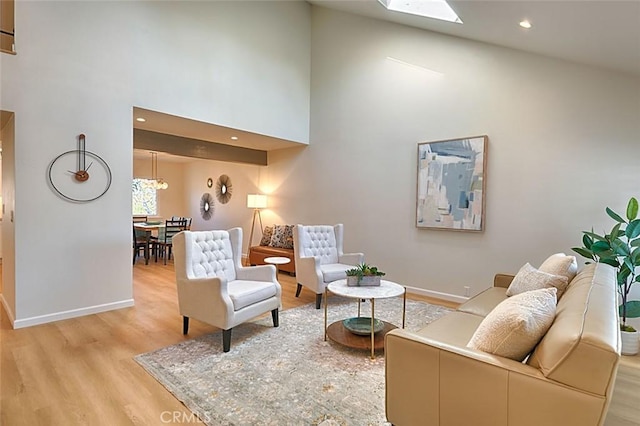 living room featuring light wood-type flooring, a skylight, and a high ceiling