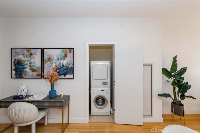 laundry area with light wood-type flooring, baseboards, and stacked washer and clothes dryer