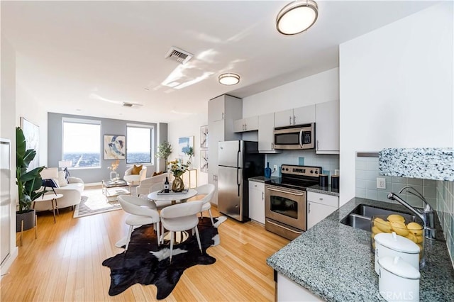 kitchen featuring tasteful backsplash, dark stone countertops, sink, light hardwood / wood-style flooring, and stainless steel appliances