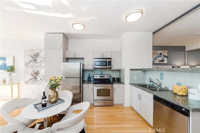 kitchen with light hardwood / wood-style floors, appliances with stainless steel finishes, backsplash, dark stone countertops, and sink