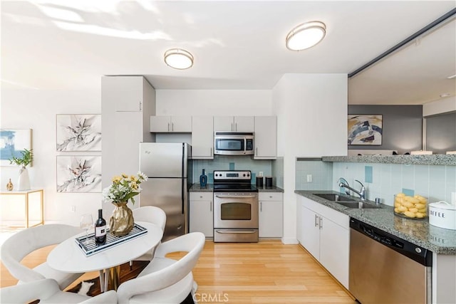 kitchen with stainless steel appliances, light wood-style flooring, a sink, dark stone counters, and tasteful backsplash