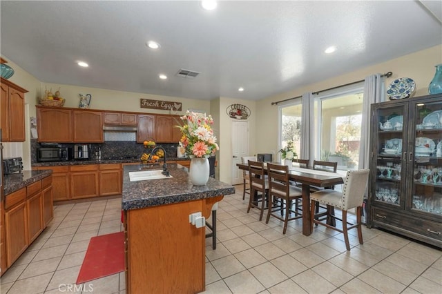 kitchen featuring tasteful backsplash, sink, light tile patterned floors, a center island with sink, and a breakfast bar area